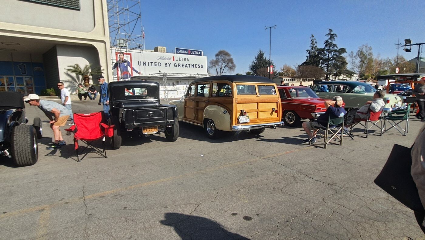 Drewniane kombi Ford Woodie z lat 40. na zlocie – obok czarnego rat roda i składanych krzeseł