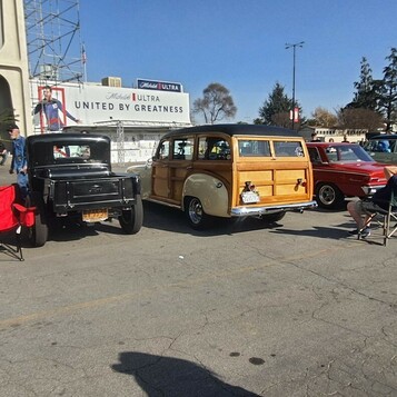 Drewniane kombi Ford Woodie z lat 40. na zlocie – obok czarnego rat roda i składanych krzeseł