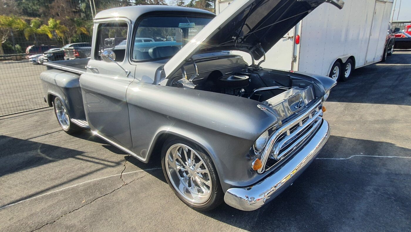 Srebrny Chevrolet 3100 Task Force z 1957 roku z otwartą maską – pickup z panoramiczną szybą