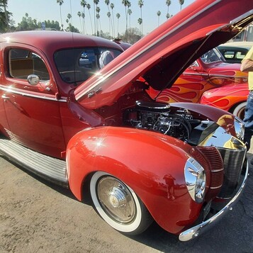 Czerwony Ford Deluxe Tudor sedan z 1940 roku z otwartą maską – dwudrzwiowy sedan na białych ściankach