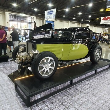 Czarno-limonkowy Ford 5-window coupe z 1932 roku na podeście – Deuce highboy w hali wystawowej
