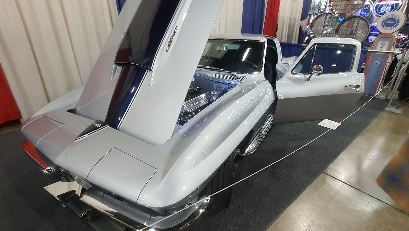 Srebrna Chevrolet Corvette Sting Ray z otwartą maską i drzwiami w hali – C2 od tyłu na stoisku