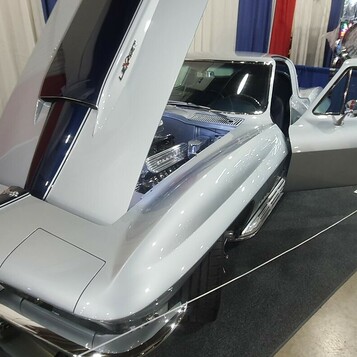 Srebrna Chevrolet Corvette Sting Ray z otwartą maską i drzwiami w hali – C2 od tyłu na stoisku