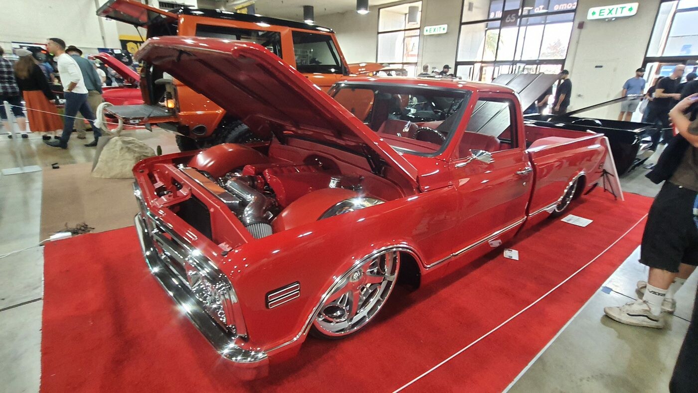 Czerwony Chevrolet C10 z 1968 roku restomod na czerwonym dywanie – otwarta maska i polerowane felgi w hali