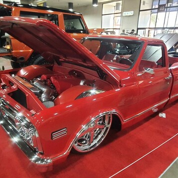 Czerwony Chevrolet C10 z 1968 roku restomod na czerwonym dywanie – otwarta maska i polerowane felgi w hali
