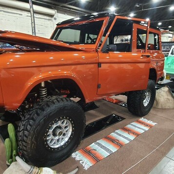 Pomarańczowy Ford Bronco pierwszej generacji na wielkich oponach – terenowa legenda w hali zlotu