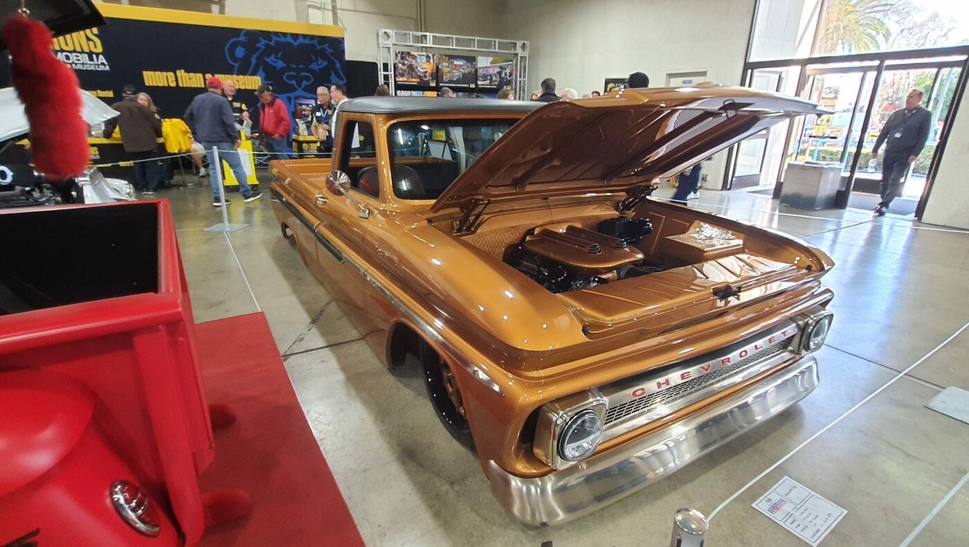 Miedziany Chevrolet C10 z 1965 roku z otwartą maską w hali – pickup w kolorze bursztynu na czerwonym dywanie