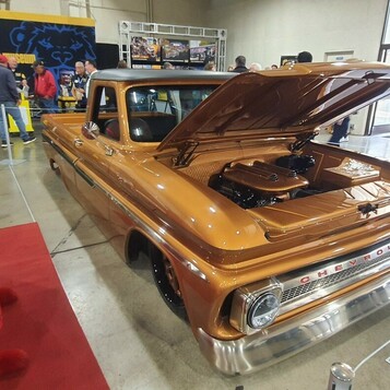 Miedziany Chevrolet C10 z 1965 roku z otwartą maską w hali – pickup w kolorze bursztynu na czerwonym dywanie