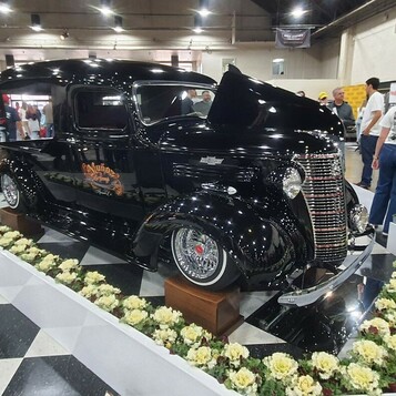 Czarny Chevrolet panel delivery z 1938 roku na szachownicy – przedwojenna furgonetka wśród kwiatów w hali