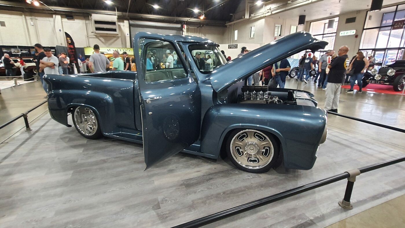 Grafitowy Ford F-100 z 1956 roku z otwartą maską i drzwiami – restomod w hali na polerowanych felgach