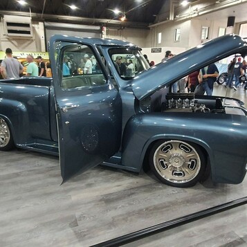 Grafitowy Ford F-100 z 1956 roku z otwartą maską i drzwiami – restomod w hali na polerowanych felgach
