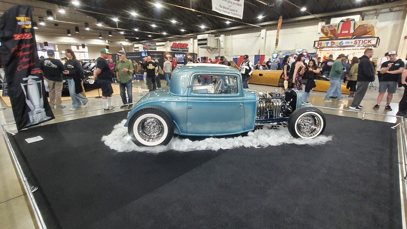 Stalowoniebieski Ford Model A coupe hot rod na „solnym” podeście – tradycyjny highboy w hali zlotu