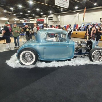 Stalowoniebieski Ford Model A coupe hot rod na „solnym” podeście – tradycyjny highboy w hali zlotu