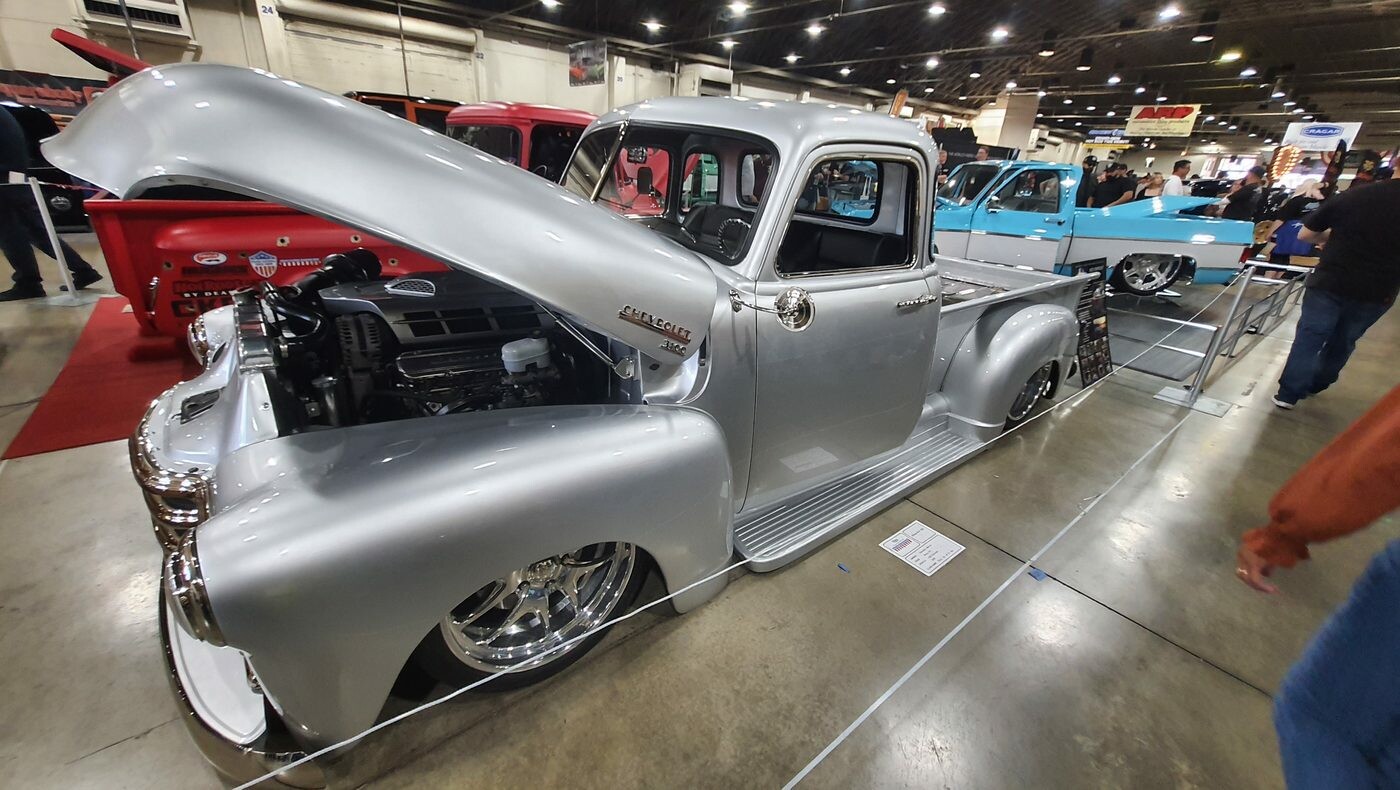 Srebrny Chevrolet 3100 Advance Design z otwartą maską – pickup na polerowanych felgach w hali zlotu