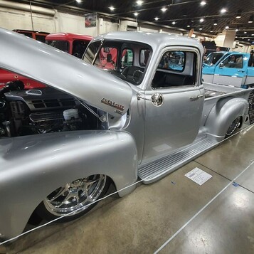 Srebrny Chevrolet 3100 Advance Design z otwartą maską – pickup na polerowanych felgach w hali zlotu