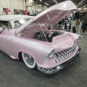 Różowy kustom z lat 50. z zębatą atrapą i białym dachem – obniżony do ziemi, z otwartą maską w hali
