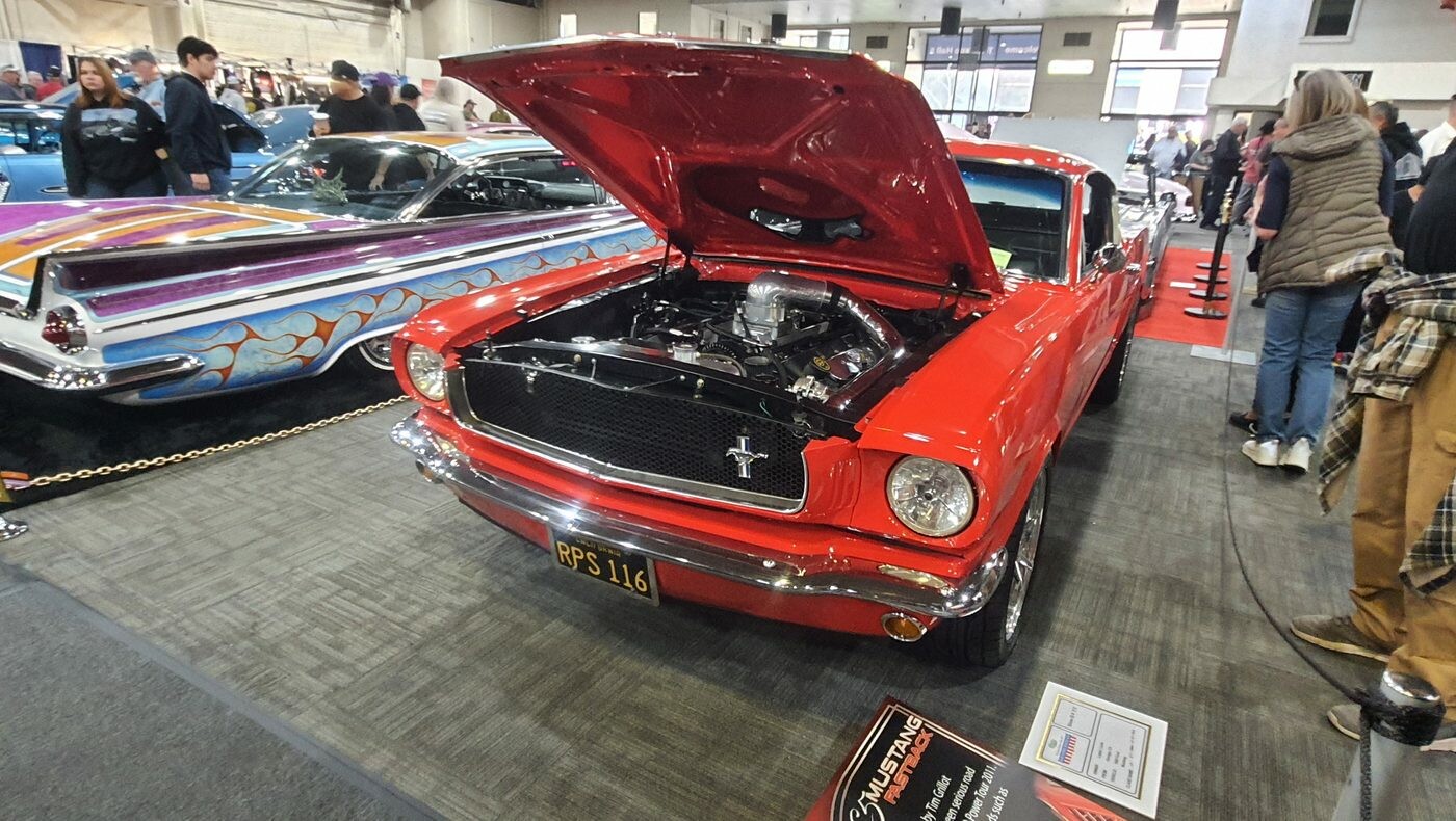 Czerwony Ford Mustang fastback z 1966 roku z otwartą maską – klasyk na czarnej tablicy z epoki w hali