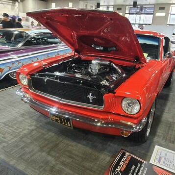 Czerwony Ford Mustang fastback z 1966 roku z otwartą maską – klasyk na czarnej tablicy z epoki w hali