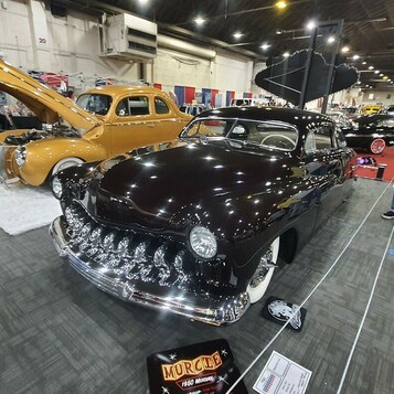 Śliwkowy Mercury z 1951 roku chopped z zębatą atrapą – lead sled na białym „śniegu” z otwartą maską w hali
