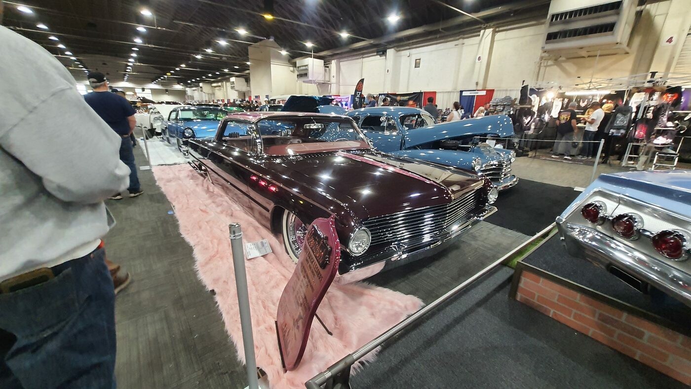 Bordowy Chevrolet Master Deluxe z 1939 roku bomb – daszek, białe ścianki i różowy dywan w hali