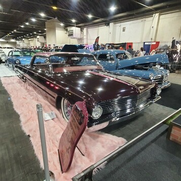 Bordowy Chevrolet Master Deluxe z 1939 roku bomb – daszek, białe ścianki i różowy dywan w hali