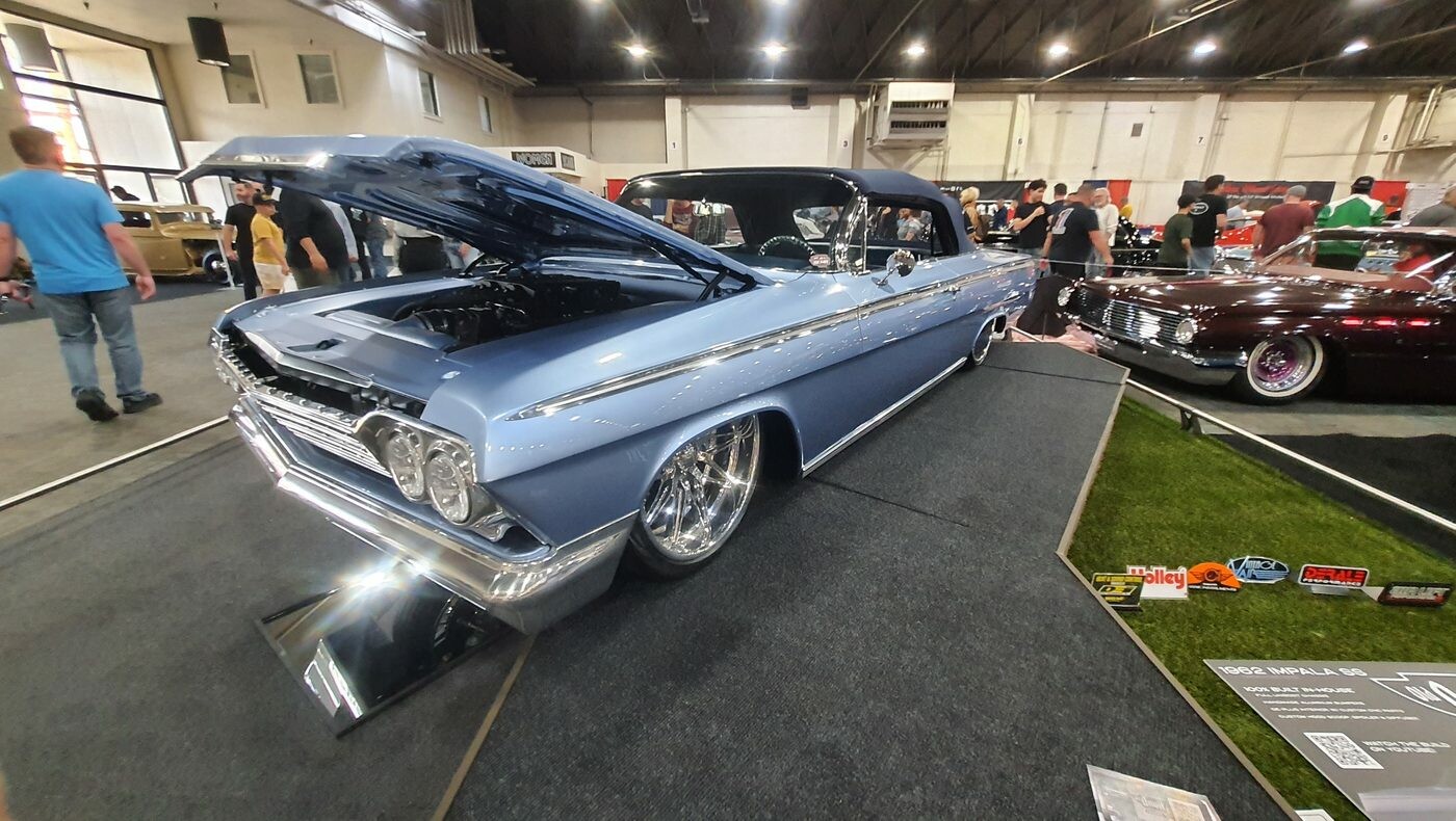 Błękitny Chevrolet Impala z 1962 roku lowrider na drucianych felgach – chrom, biel i błękit w hali zlotu