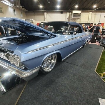 Błękitny Chevrolet Impala z 1962 roku lowrider na drucianych felgach – chrom, biel i błękit w hali zlotu