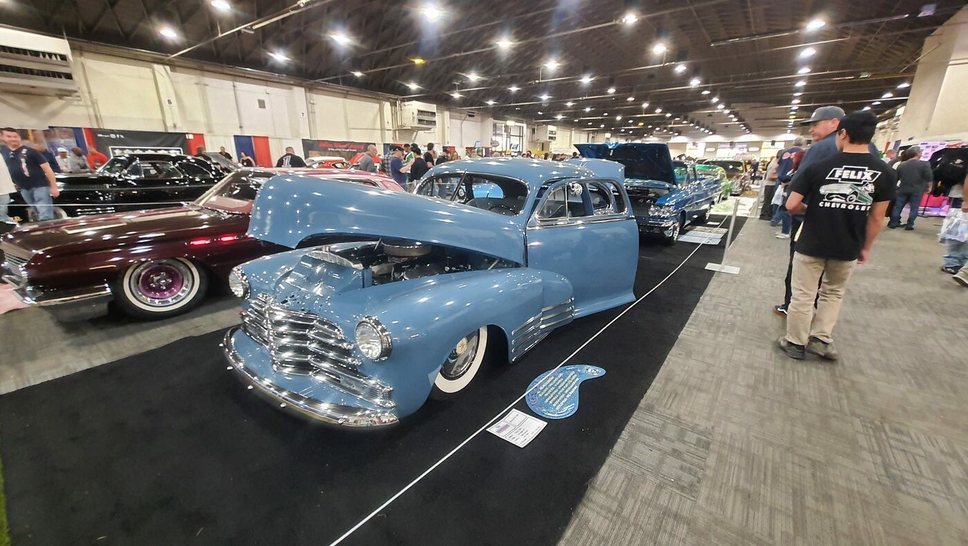 Błękitny Chevrolet Fleetline z 1948 roku bomb z otwartą maską – fastback z daszkiem na białych ściankach w hali