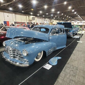 Błękitny Chevrolet Fleetline z 1948 roku bomb z otwartą maską – fastback z daszkiem na białych ściankach w hali