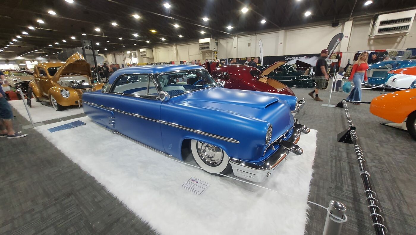 Satynowo-niebieski Mercury Monterey z 1953 roku chopped – kustom na białym futrze w hali zlotu