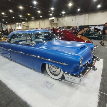 Satynowo-niebieski Mercury Monterey z 1953 roku chopped – kustom na białym futrze w hali zlotu
