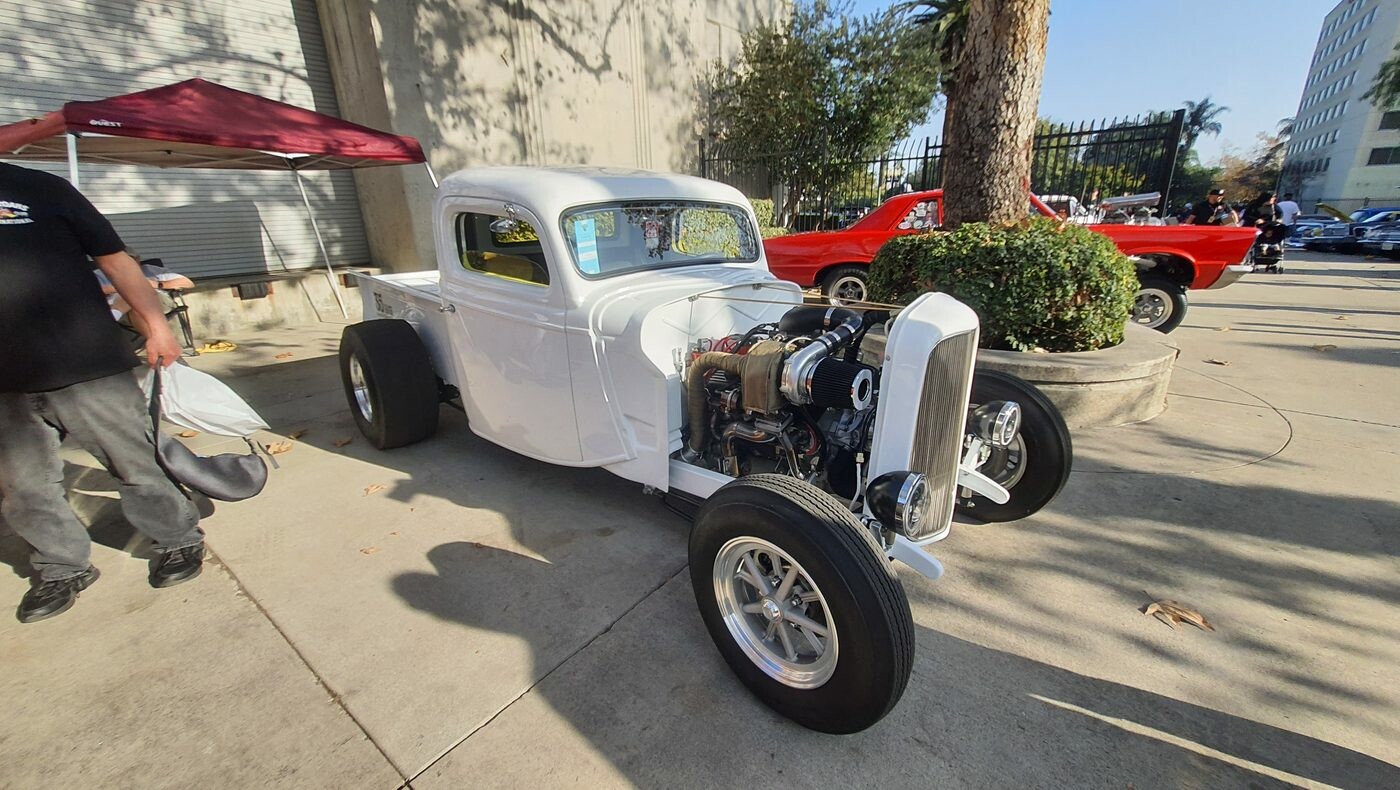Biały Ford pickup z 1936 roku z odsłoniętym silnikiem – hot rod użytkowy na polerowanych felgach przed halą