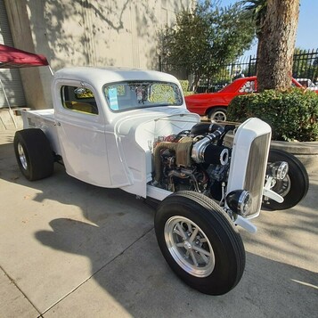 Biały Ford pickup z 1936 roku z odsłoniętym silnikiem – hot rod użytkowy na polerowanych felgach przed halą