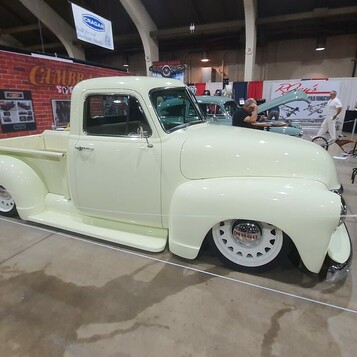 Kremowy Chevrolet 3100 Advance Design na białych ściankach – pickup w pastelowej bieli na stoisku z ceglaną ścianą