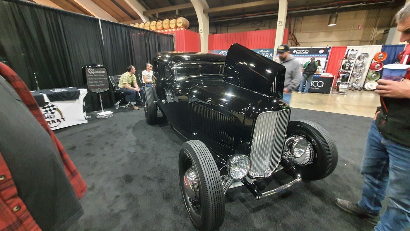 Czarny Ford roadster z 1932 roku na stoisku w hali – Deuce highboy w lustrzanej czerni na czarnych felgach