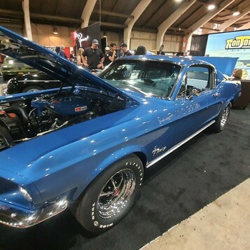 Niebieski Ford Mustang fastback z 1968 roku z otwartą maską – Acapulco Blue na stoisku w hali zlotu