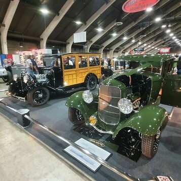 Zielony Ford 5-window coupe z 1932 roku w pełnych błotnikach obok woodie – Deuce w kolorze lasu na podeście w hali