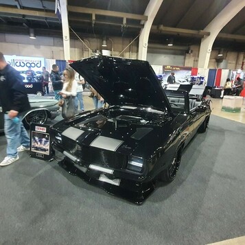 Czarny Chevrolet Camaro kabriolet z 1969 roku ze srebrnymi pasami – pro touring z otwartą maską w hali