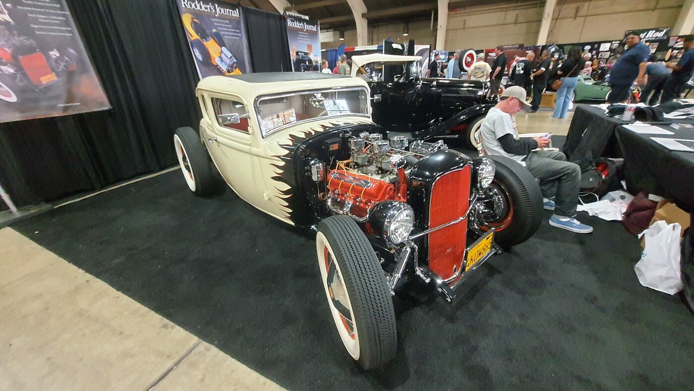 Biały Ford Model A coupe z czerwonymi felgami i czerwonym silnikiem – tradycyjny hot rod na stoisku Rodder's Journal