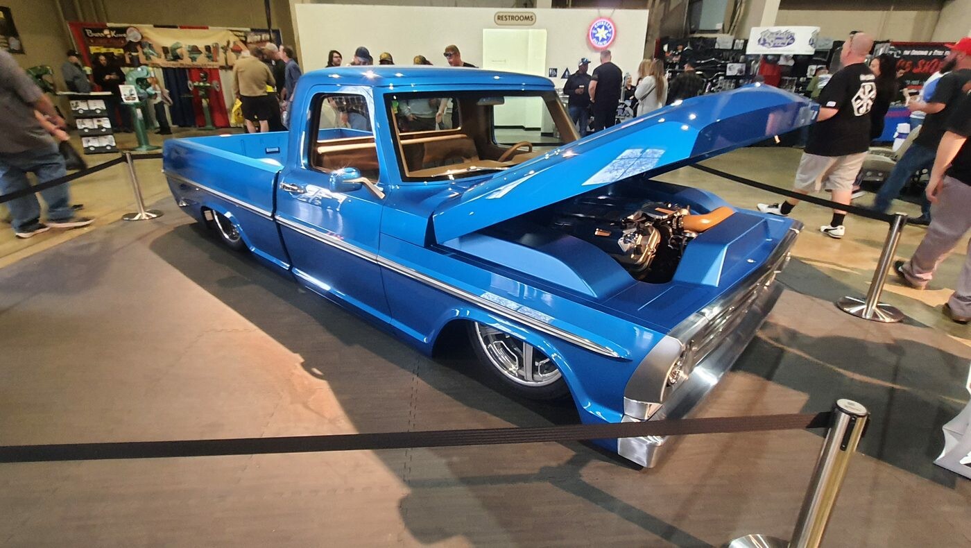 Niebieski Ford F-100 z 1976 roku z otwartą maską – „dentside” na polerowanych felgach w głównej hali