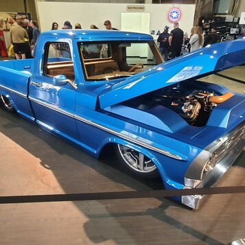 Niebieski Ford F-100 z 1976 roku z otwartą maską – „dentside” na polerowanych felgach w głównej hali