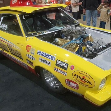 Żółty Ford Mustang II Pro Stock z lat 70. – drag car z naklejkami sponsorów i silnikiem bez maski w hali